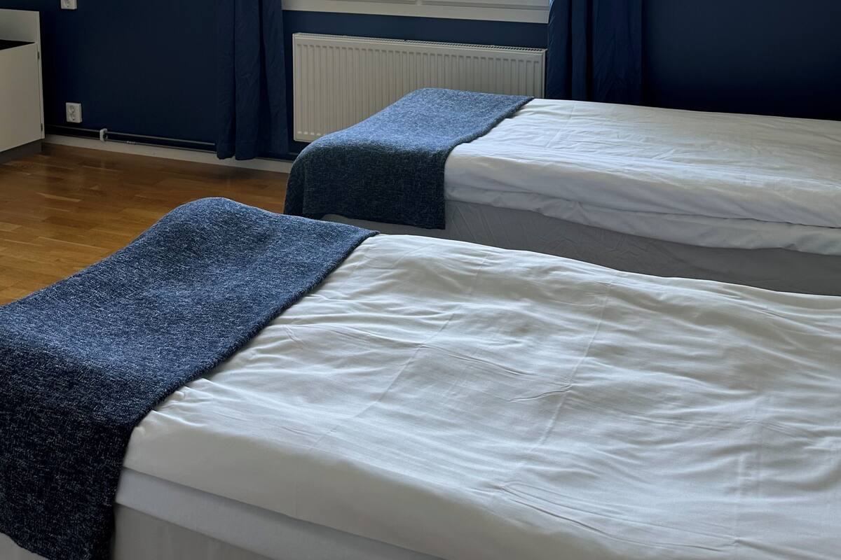 Une chambre avec deux lits, une fenêtre avec des rideaux, un radiateur et un porte-manteau fixé au mur.
