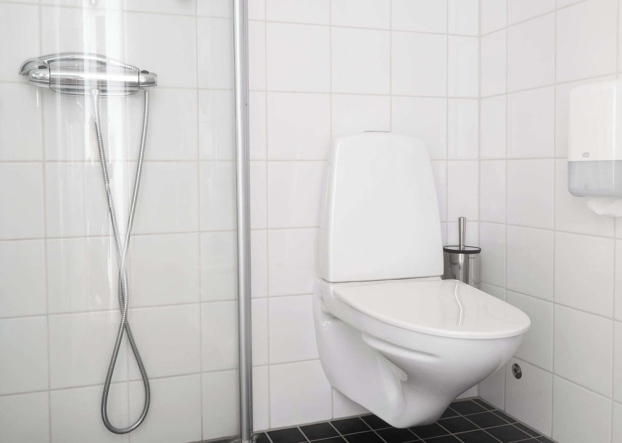 Un baño moderno con inodoro blanco, cabina de ducha de cristal y secamanos.
