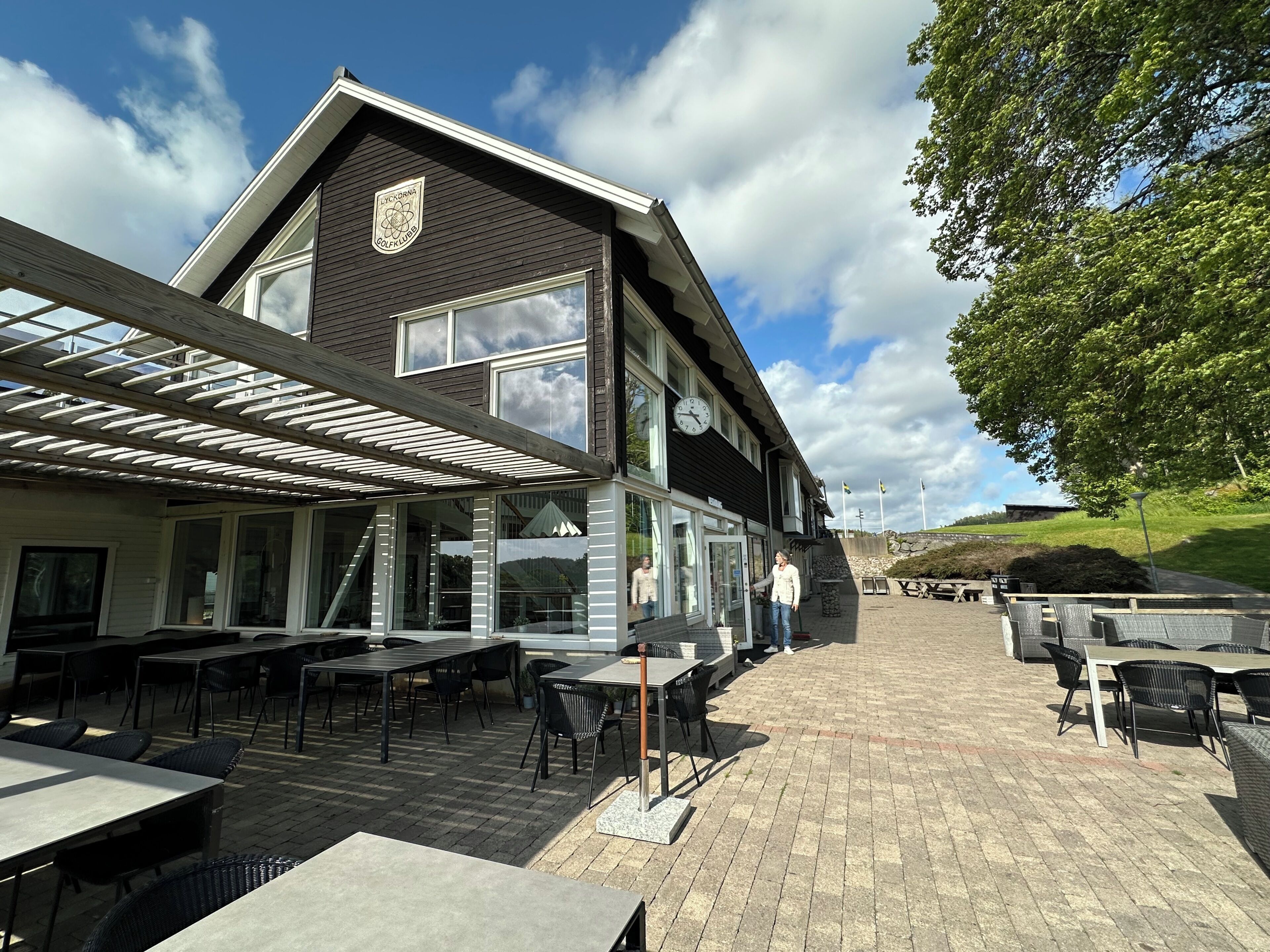 En byggnad med en logotyp, stora fönster, utomhusplatser och en stenlagd uteplats.