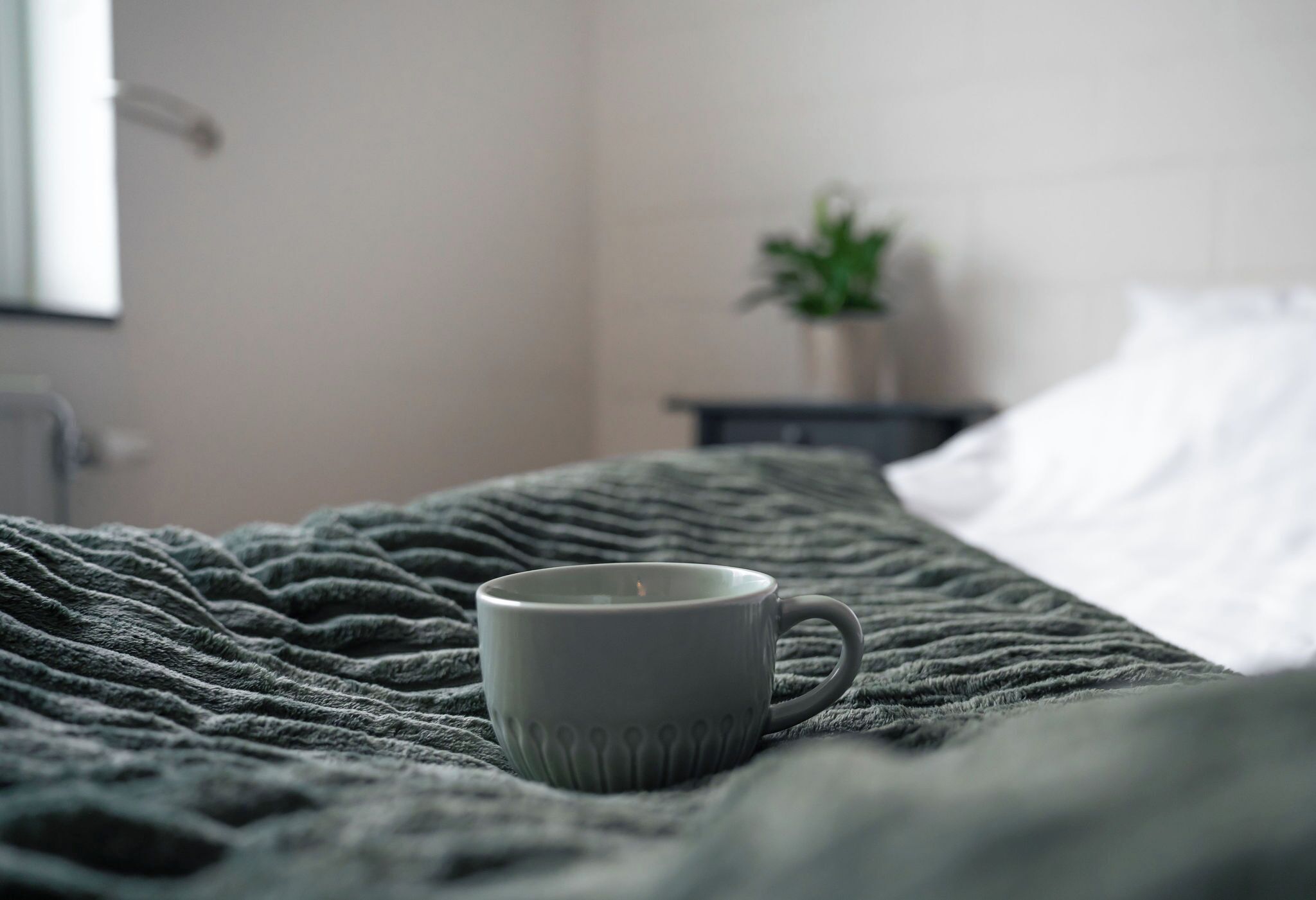 Un lit avec une couverture verte et une tasse grise posée dessus.