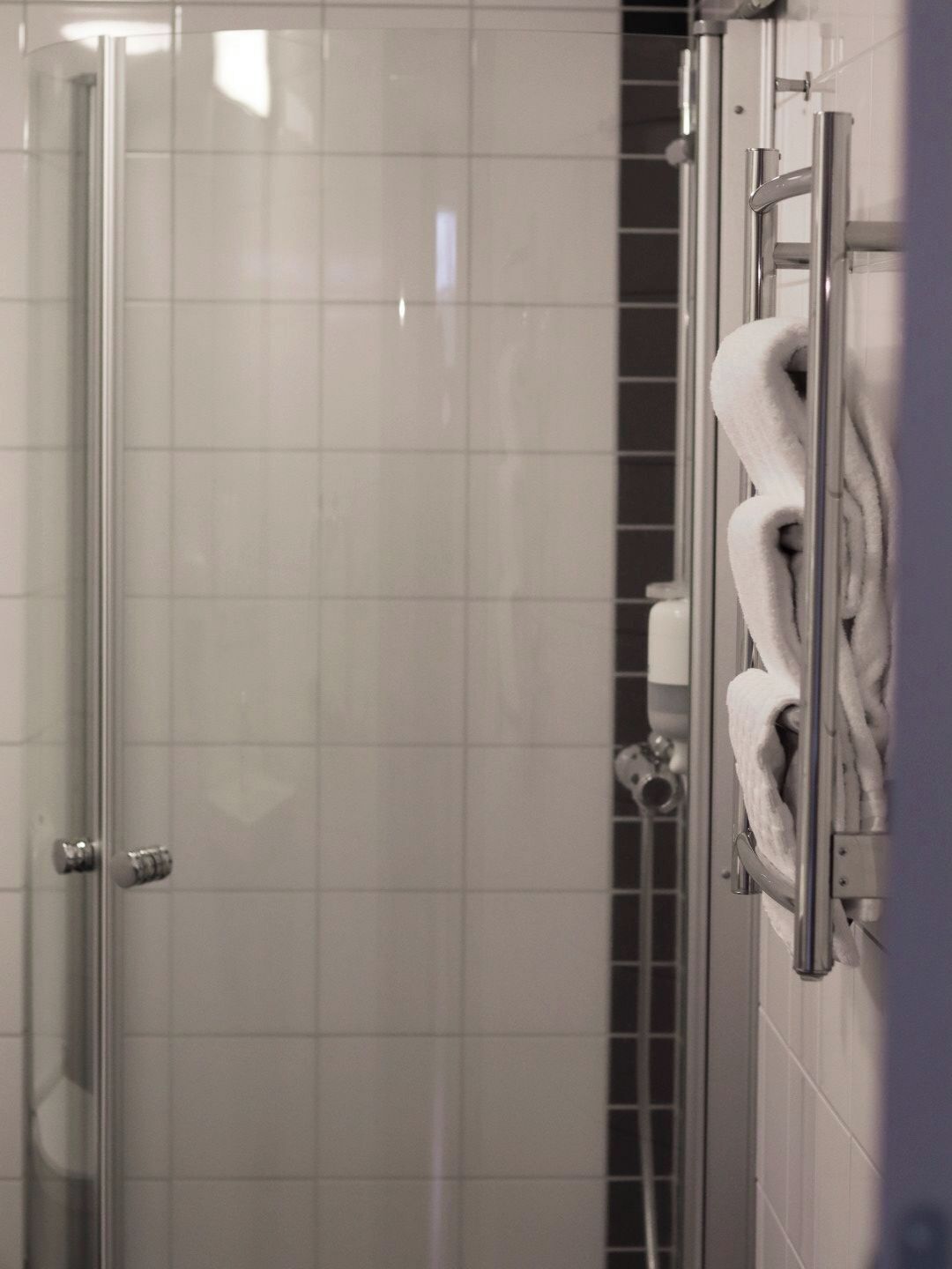 A glass-enclosed shower with a tiled wall, a towel rack with a towel, and a showerhead.