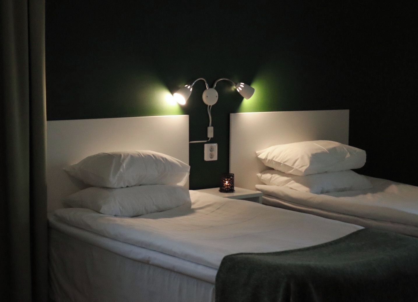 A twin room with two single beds, a nightstand, and a wall-mounted lamp.