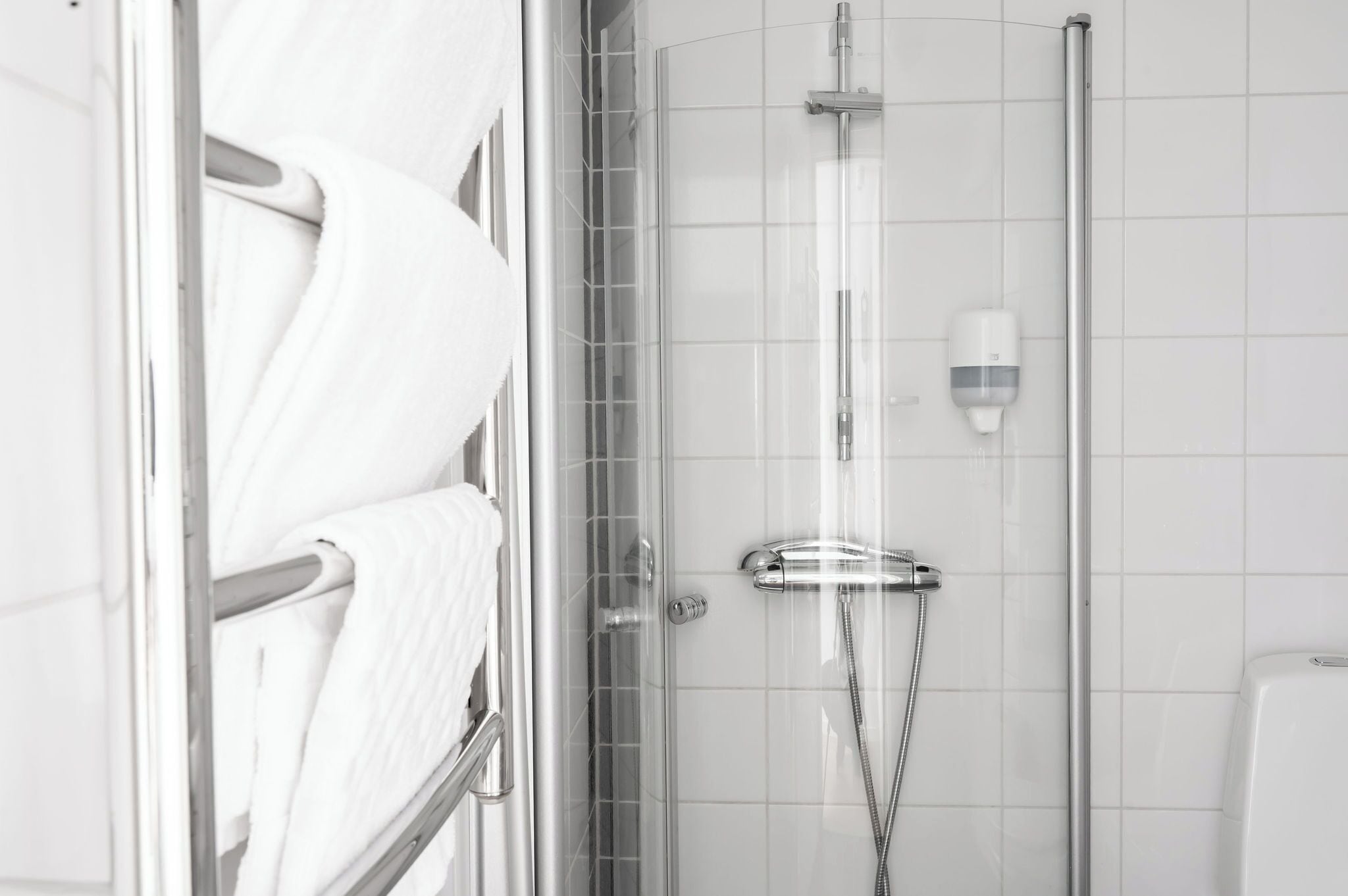 Un baño moderno con cabina de ducha de vidrio, un perchero con toallas blancas y un dispensador de jabón en la pared.