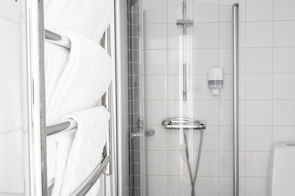 Un baño moderno con cabina de ducha de vidrio, un perchero con toallas blancas y un dispensador de jabón en la pared.