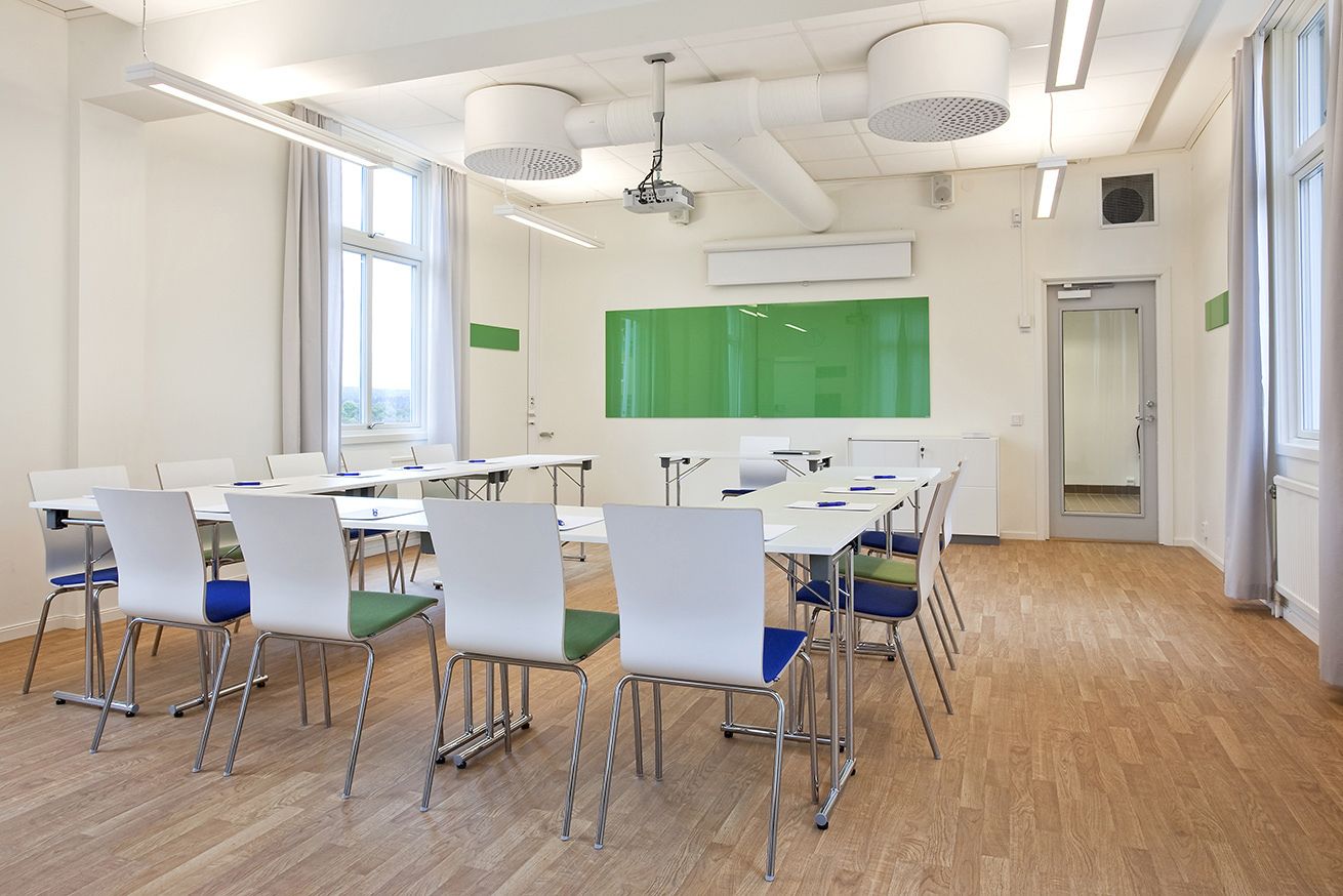 A classroom with white tables and chairs, a green screen, and a projector.