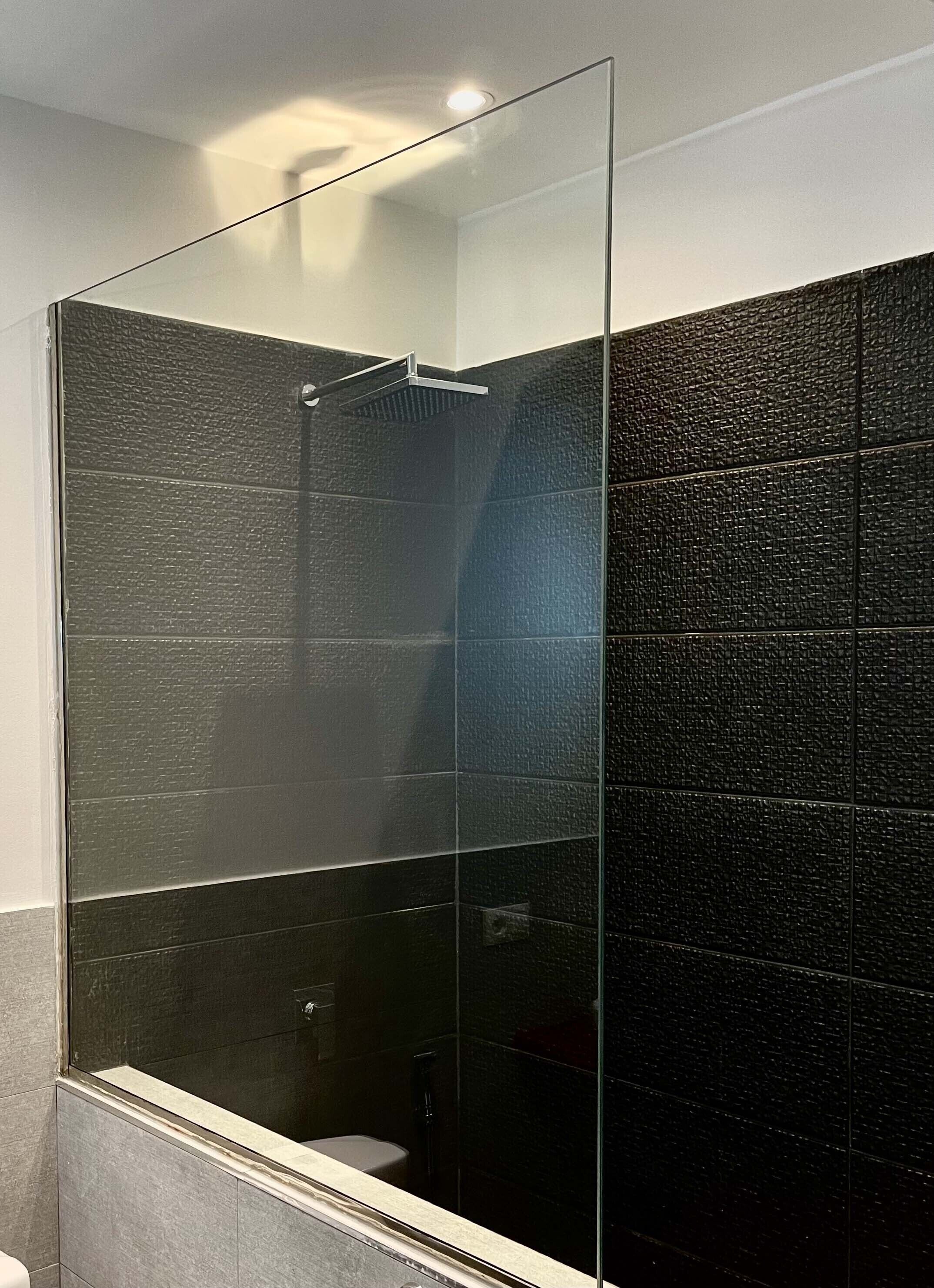 A modern bathroom with a glass shower enclosure, dark textured walls, and a visible toilet.
