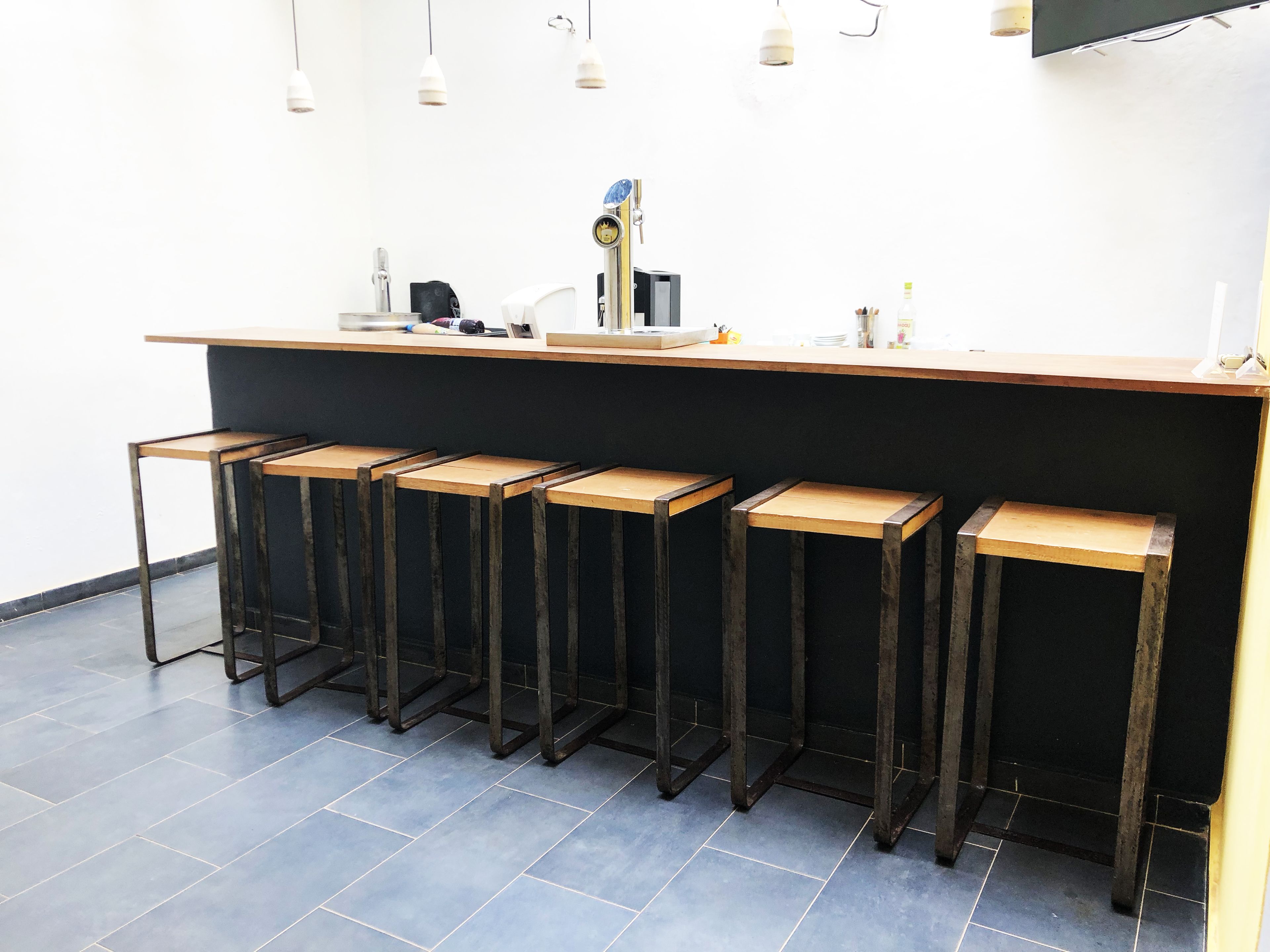 A bar area with a black countertop, five wooden stools, and a clock above the bar.
