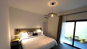 A modern hotel room with a large bed, a ceiling light fixture, and a view of the outdoors through a sliding glass door. - Hotel du Phare (Dakar)