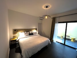 Habitación de hotel moderna con una cama grande, una lámpara colgante y vistas al exterior a través de una puerta corrediza de vidrio.