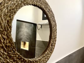 Un baño con espejo tejido, toallero y pared de azulejos.