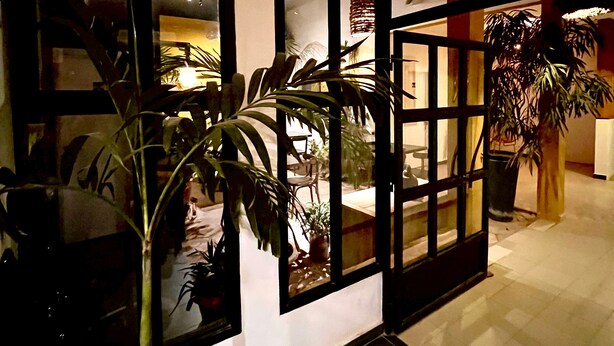 A room with a tiled floor, a potted plant, a chair, and a window with a view of the outside. - Hotel du Phare (Dakar)