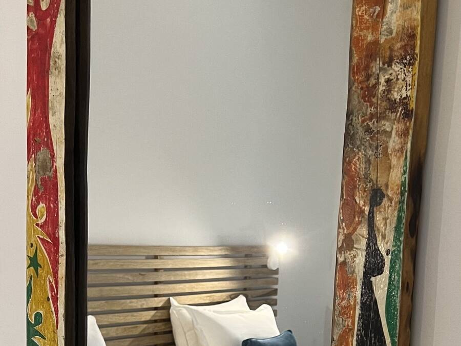 Un dormitorio con cabecera de madera, ropa de cama blanca y un marco de espejo colorido.