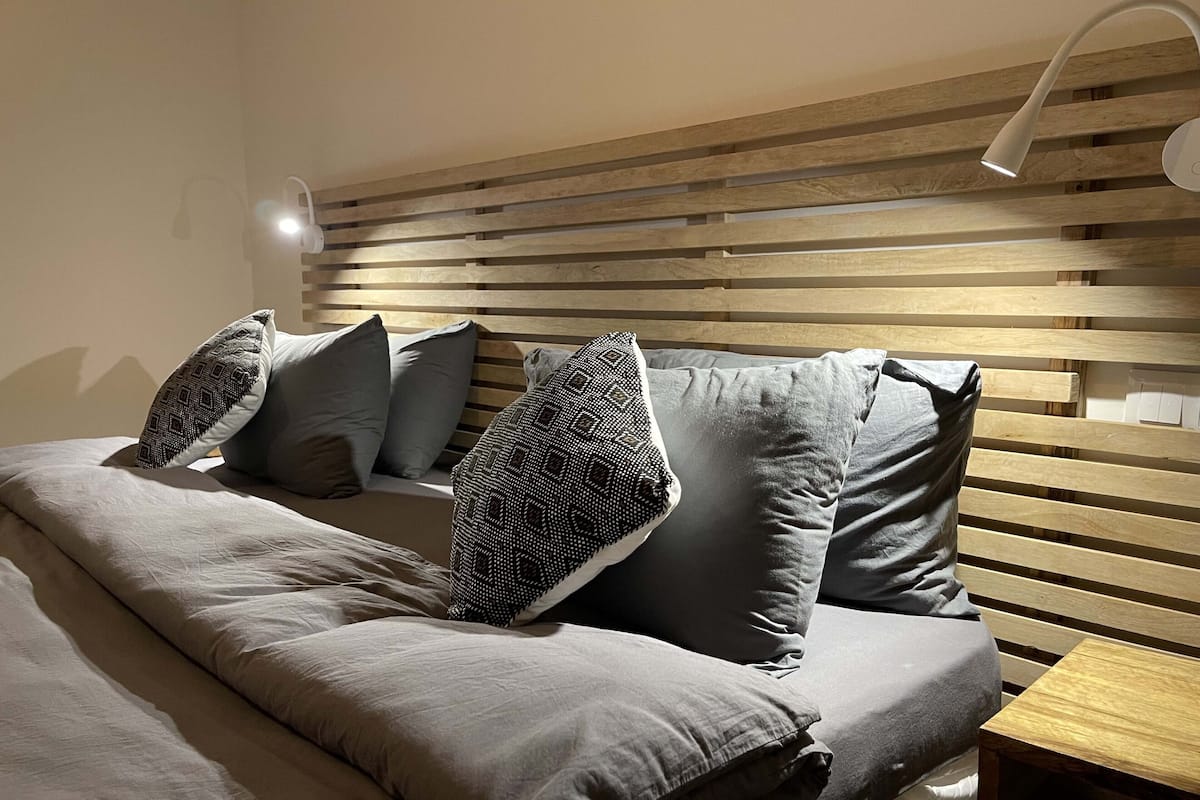 A neatly made bed with a wooden headboard, multiple pillows, and a bedside table.
