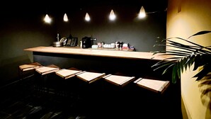 A modern bar area with a long counter, multiple stools, and pendant lighting. - Hotel du Phare (Dakar)
