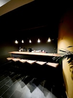 Zona de bar moderna con una barra larga, varios taburetes e iluminación colgante.