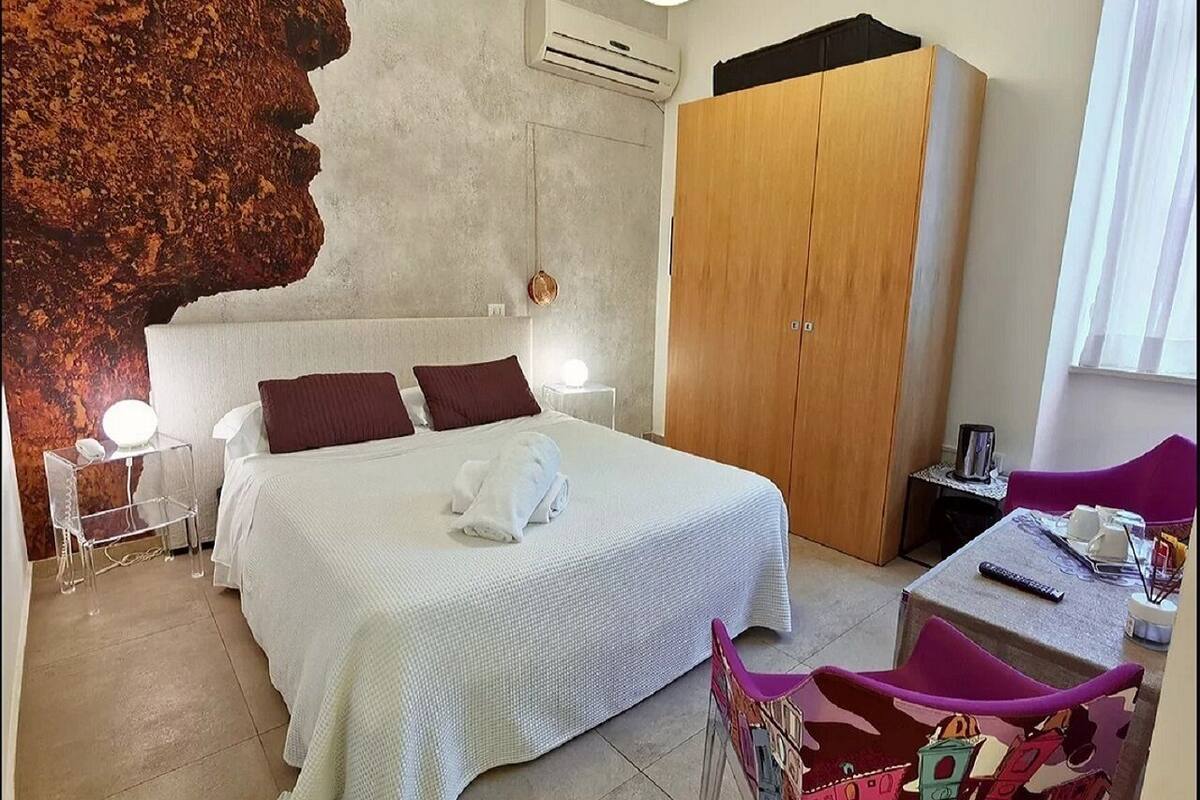 A hotel room with a large bed, a wardrobe, a desk with a chair, and a wall mural.