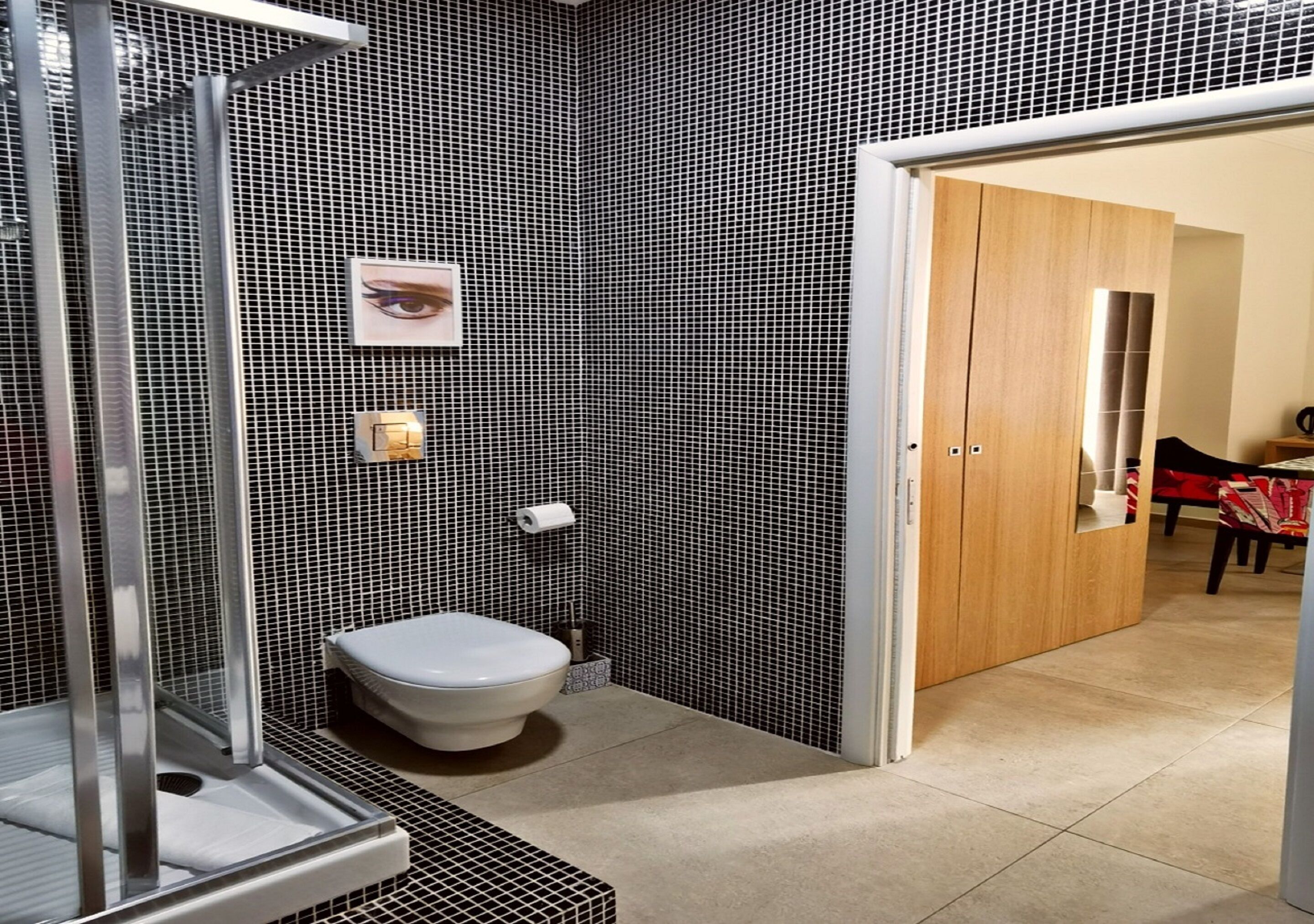 Un bagno moderno con parete rivestita in piastrelle bianche e nere, un water, zona doccia e una porta in legno che dà su un'area pranzo.