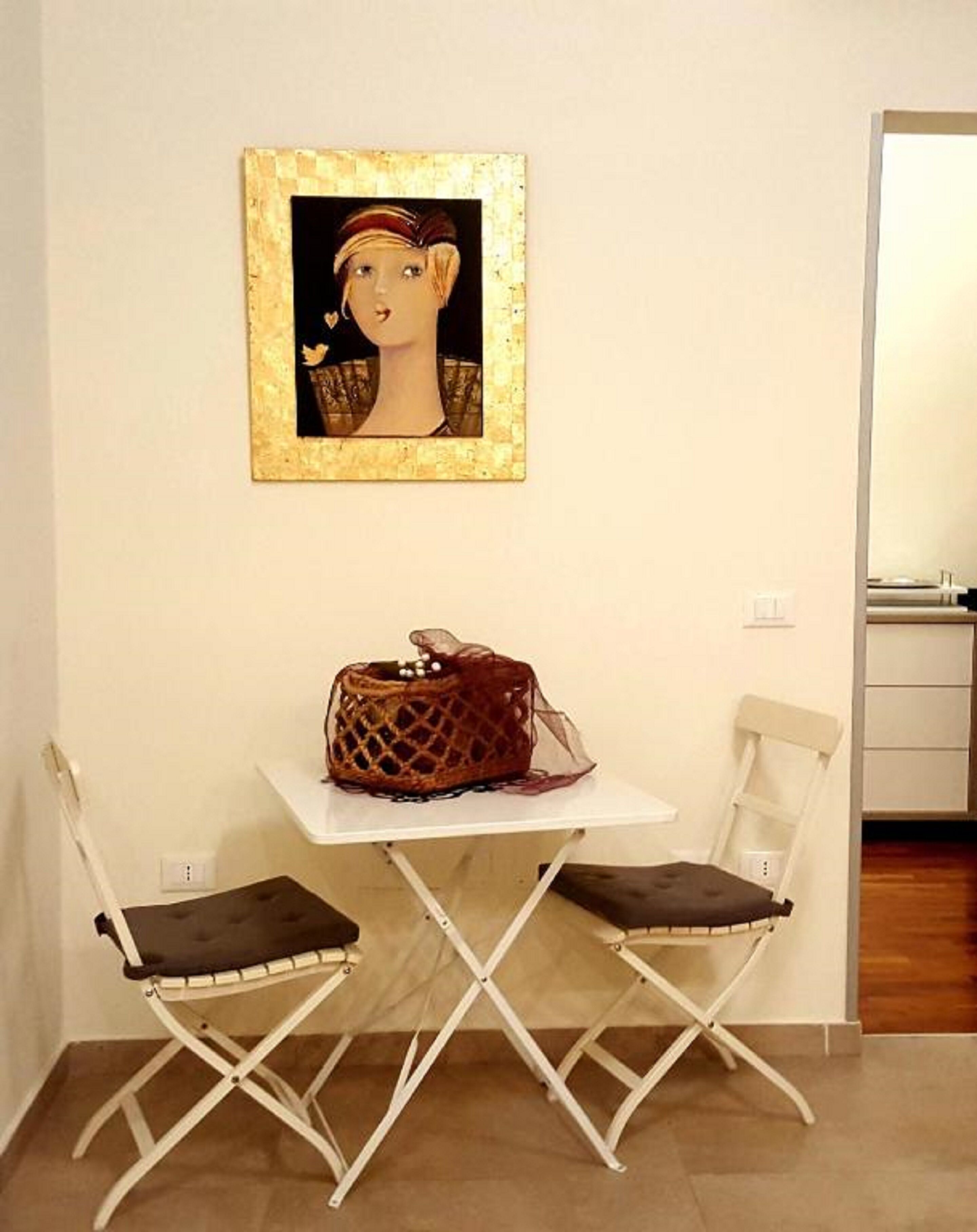 Una habitación pequeña con una mesa blanca, dos sillas, un cuadro en la pared y un bolso sobre la mesa.