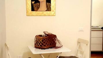 Una habitación pequeña con una mesa blanca, dos sillas, un cuadro en la pared y un bolso sobre la mesa.