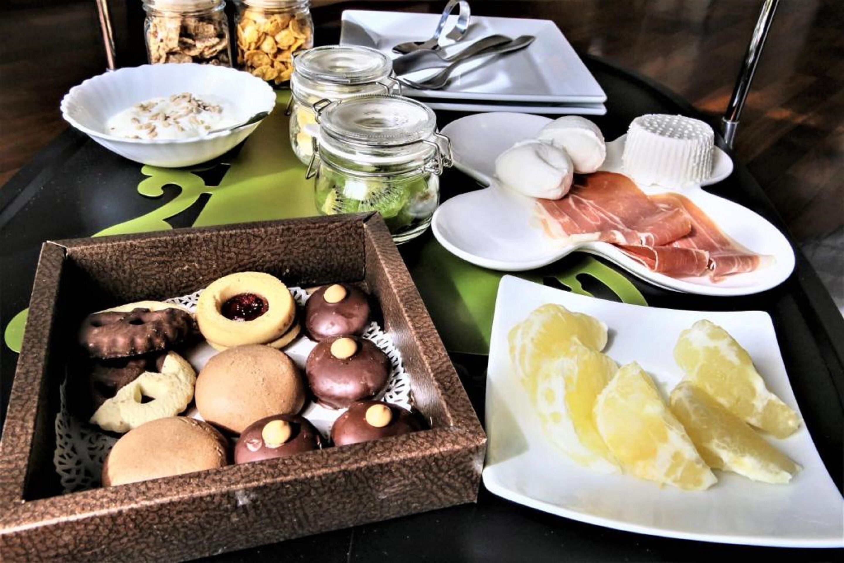 Una bandeja con diversos bocadillos como galletas, frutos secos y frutas deshidratadas, además de un plato de rodajas de limón y un recipiente con jamón serrano.
