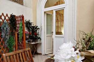 A wooden bench, a white door, and various potted plants.