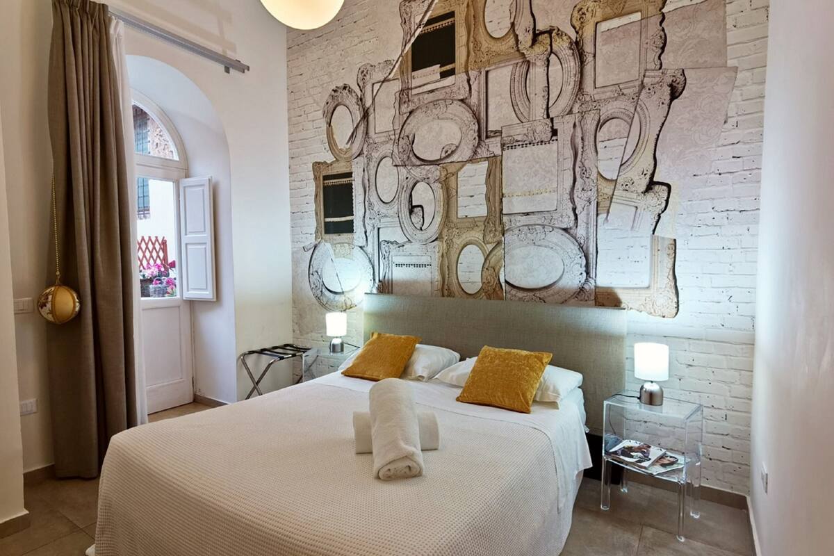 A hotel room with a large bed, two bedside tables with lamps, a decorative wall mural, and a window with curtains.