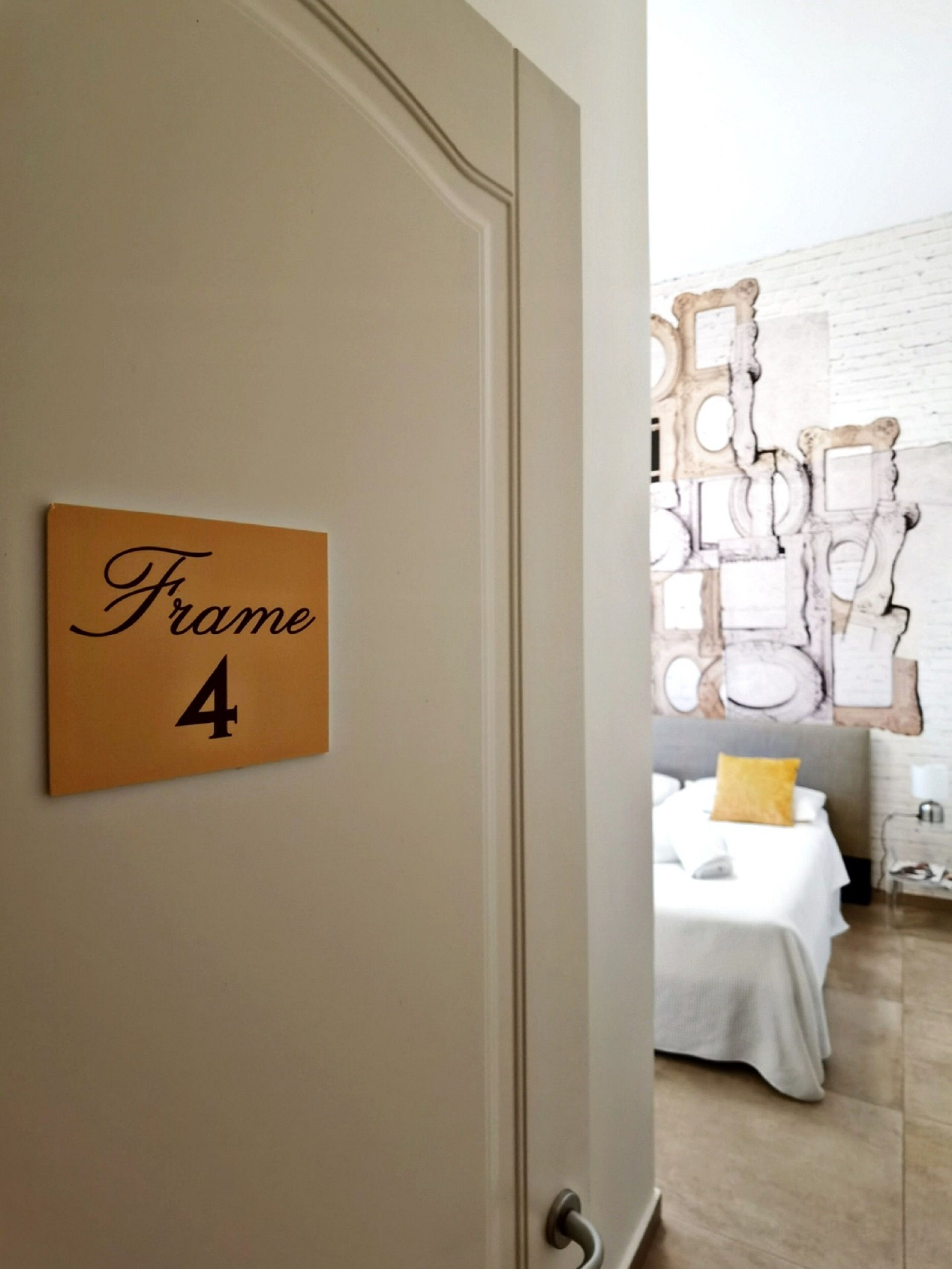 Une chambre d’hôtel avec un lit, une table de chevet et un mur orné d’un miroir décoratif. Une inscription sur le mur indique : « Cadre 4 ».