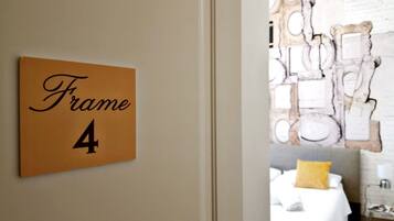 Une chambre d’hôtel avec un lit, une table de chevet et un mur orné d’un miroir décoratif. Une inscription sur le mur indique : « Cadre 4 ».