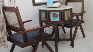 A dining area with a table and two chairs, a window with curtains, and a wall-mounted light fixture. - Garden Lodge (Zanzibar Town)
