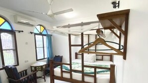 A room with a bed, a desk, a chair, and a hanging coat rack. - Garden Lodge (Zanzibar Town)