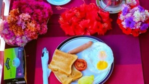 A table set with breakfast items including toast, eggs, and sausages, with a thermos, plates, and a box of Kleenex. - Garden Lodge (Zanzibar Town)