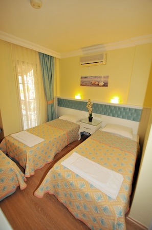 A hotel room with two beds, a nightstand, an air conditioning unit, and a window with curtains. - Ilkiz Beach Hotel (Fethiye)