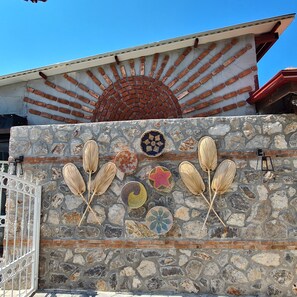 Un mur de pierre agrémenté de panneaux décoratifs en fibres tressées et une porte en métal.