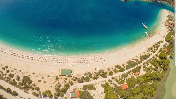 An aerial view of a coastal area with a beach, a small island, and a boat. - Ilkiz Beach Hotel (Fethiye)