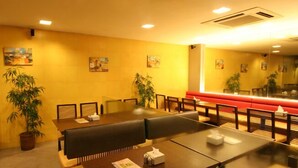 A restaurant with wooden tables and benches, potted plants, and artwork on the walls. - Jayaleela dormitory (Mumbai)