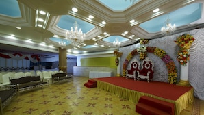 A banquet hall with a stage, seating, and chandeliers. - Jayaleela dormitory (Mumbai)