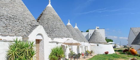A row of white buildings with conical roofs, potted plants, and outdoor seating.