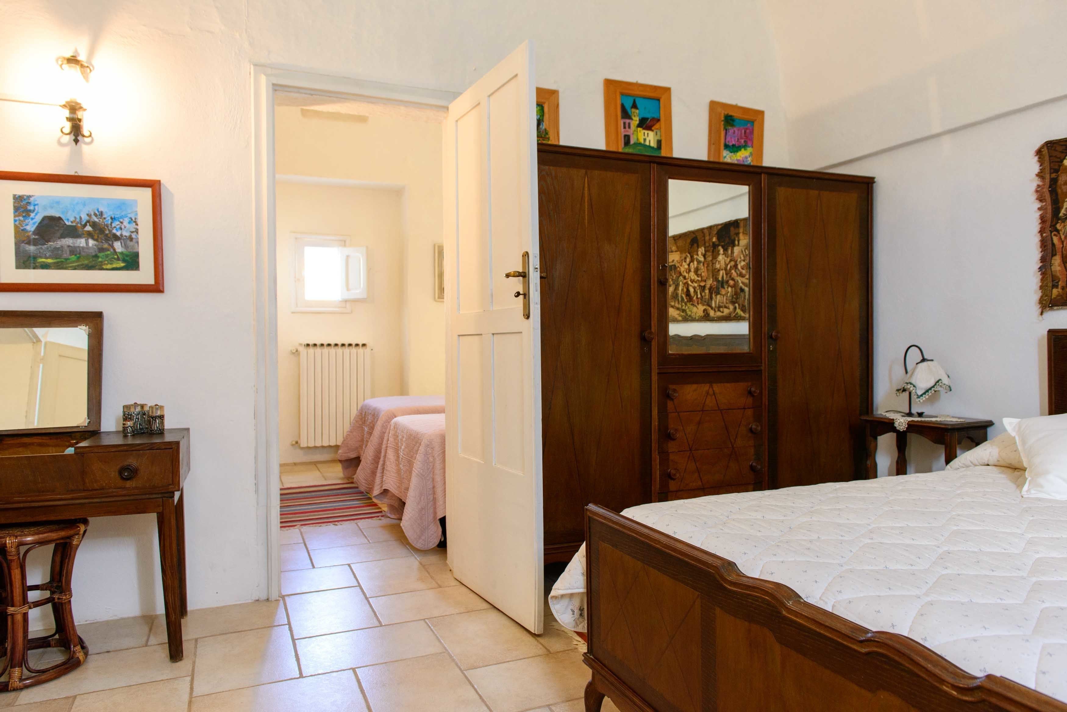 A bedroom with a wooden bed, a dresser, a mirror, and a wardrobe. There are two bedside tables and a radiator in the background.