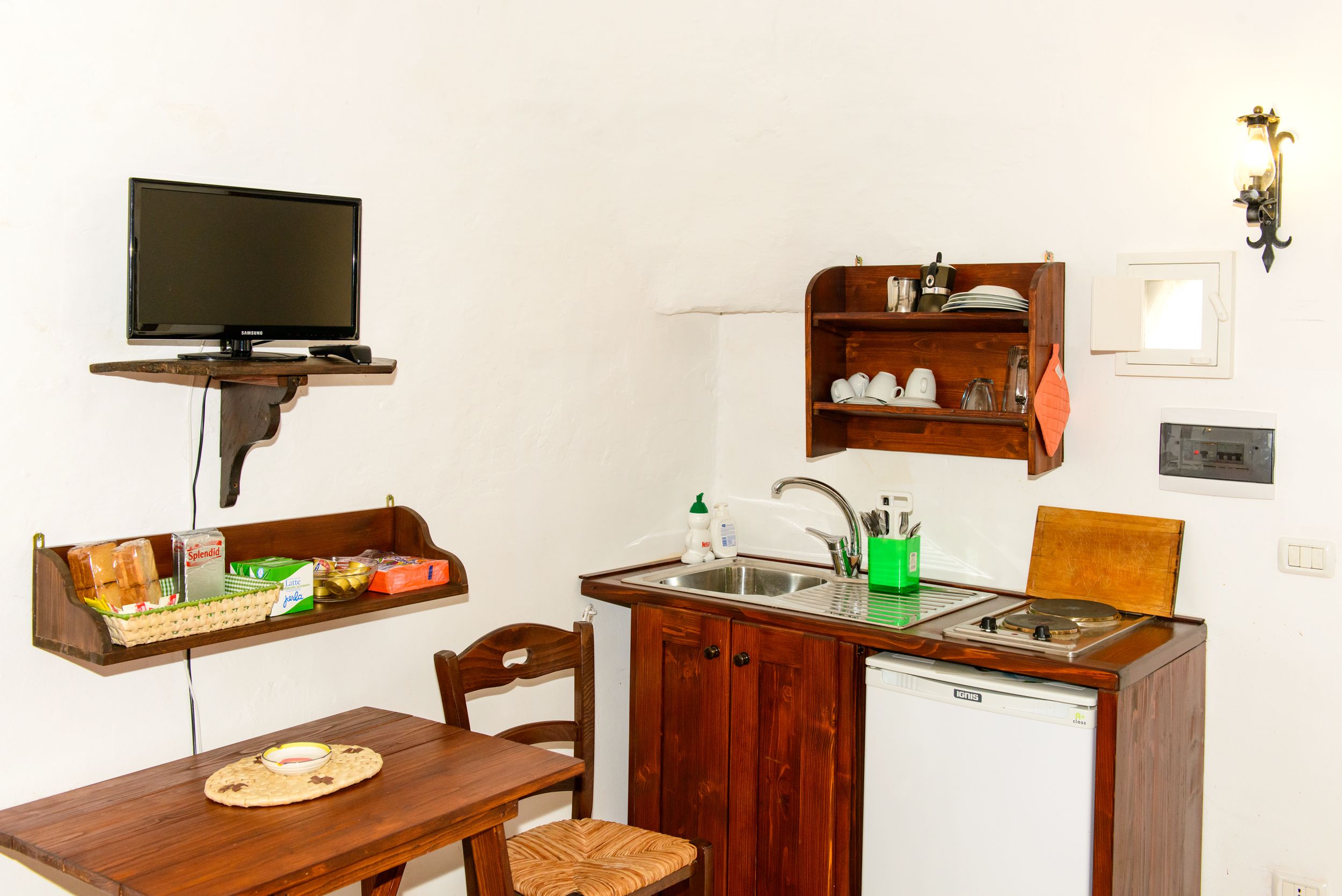 A compact kitchen with a built-in dishwasher, a wooden table, and a shelf with dishes and a kettle.