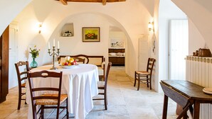 A dining area with a round table, chairs, and a white tablecloth. There is a vase with flowers on the table. - Masseria Pozzo Tre Pile  (Martina Franca)