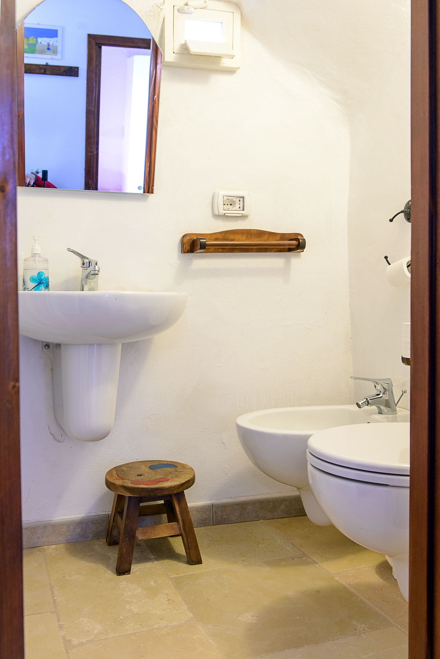 A bathroom with a pedestal sink, a toilet, and a wooden stool.