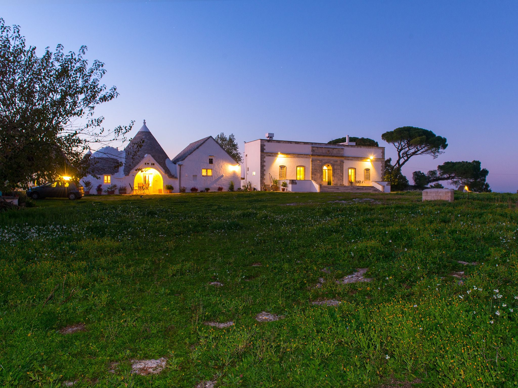 A two-story house with a stone facade, a large front lawn, and a driveway leading to a parked car.