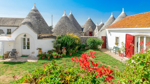 A row of traditional conical-roofed houses with a garden in the foreground. - Masseria Pozzo Tre Pile  (Martina Franca)