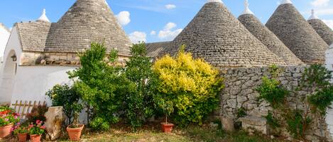 A row of traditional stone-roofed buildings with a white wall and potted plants in front.
