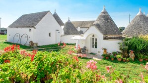 A white building with conical roofs, a small patio with a table and chairs, and potted plants in the foreground. - Masseria Pozzo Tre Pile  (Martina Franca)