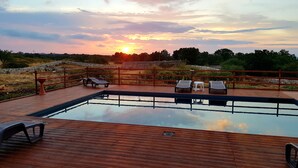 A wooden deck with a swimming pool, lounge chairs, and a view of the sunset. - Masseria Pozzo Tre Pile  (Martina Franca)