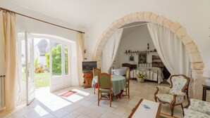 A dining area with a table and chairs, a television, and a view of the garden through an open door. - Masseria Pozzo Tre Pile  (Martina Franca)