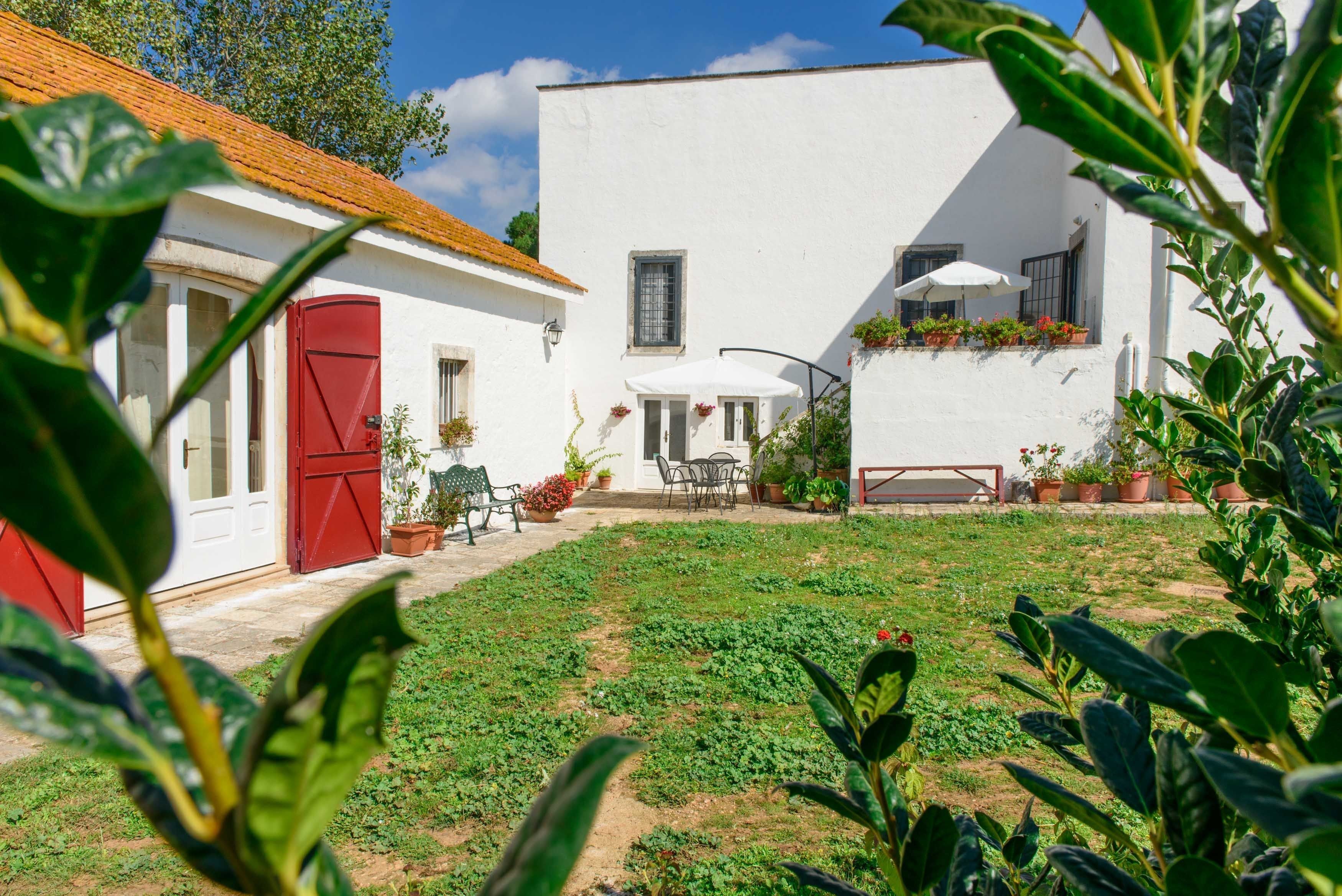 Un edificio blanco con puerta roja, un patio con mobiliario exterior y plantas en macetas.