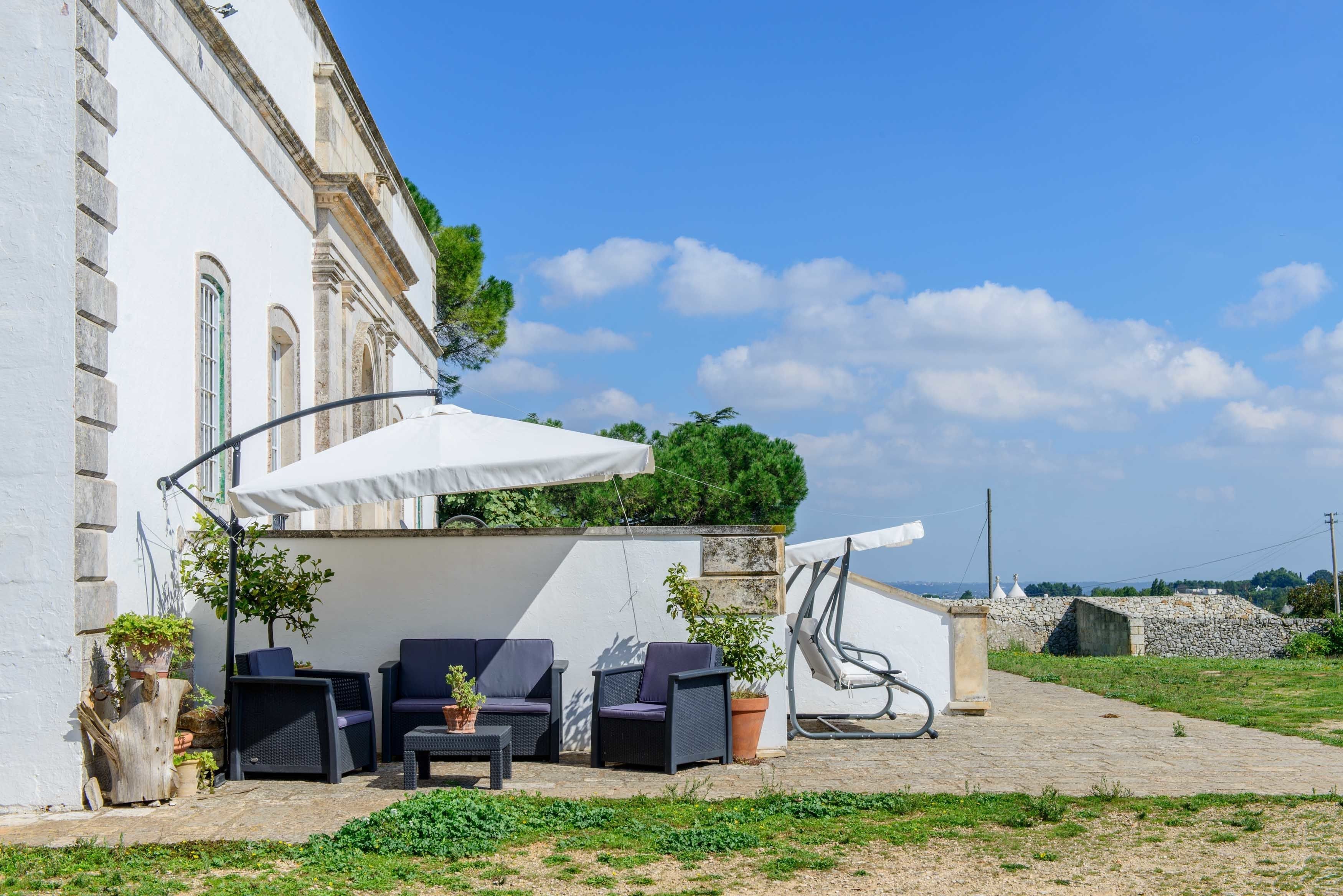 Un patio con mobiliario exterior, una sombrilla blanca y un muro de piedra.