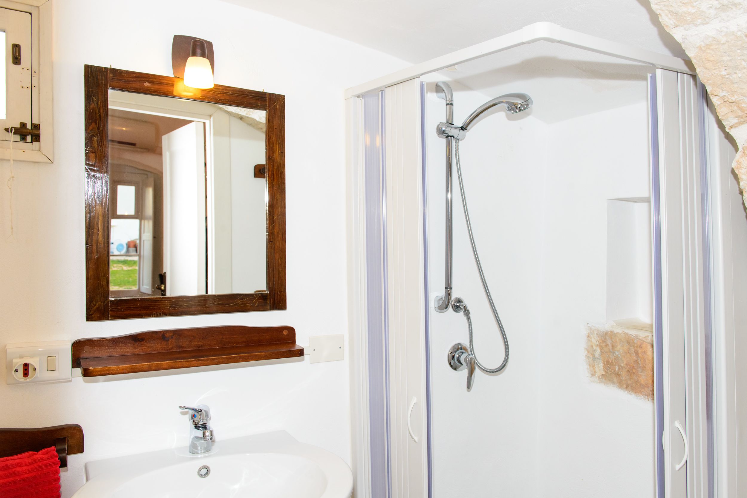 A bathroom with a white sink, a wooden vanity, a mirror, and a glass-enclosed shower.